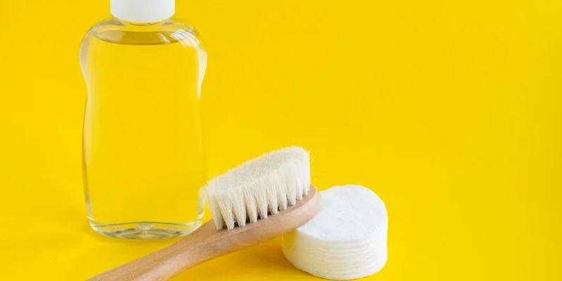 Clear glass bottle, brush, and cotton pads on a vibrant yellow background