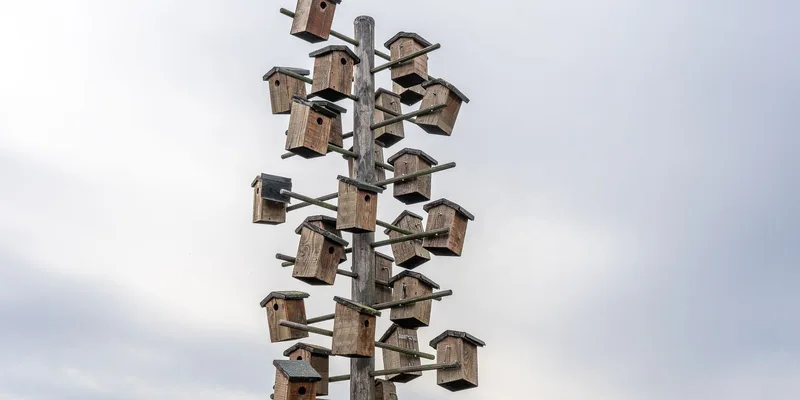 Array of birdhouses mounted on a tall wooden pole under a cloudy sky