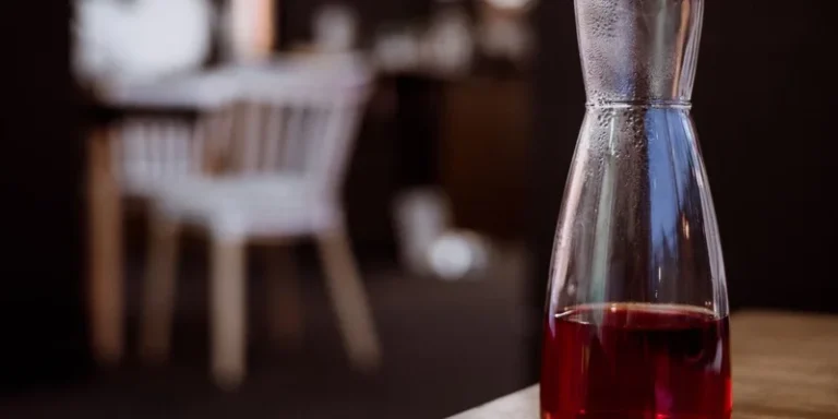 Close-up of a glass carafe filled with red liquid on a wooden table in a cozy indoor setting