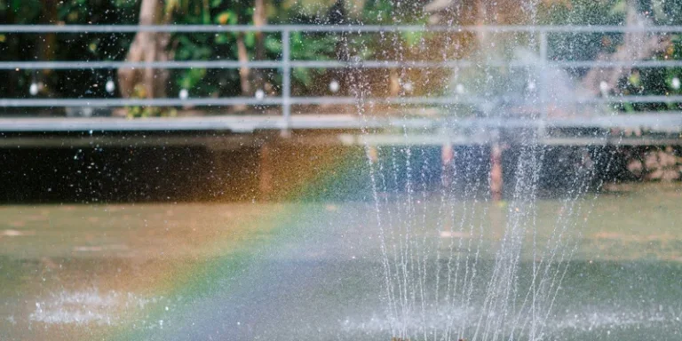 Vibrant rainbow forms as sunlight hits the spray of a water fountain outdoors