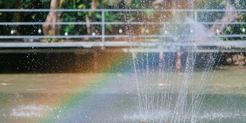 Vibrant rainbow forms as sunlight hits the spray of a water fountain outdoors
