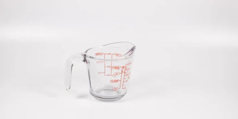 A clear glass measuring cup with red markings on a white background