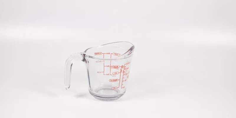 A clear glass measuring cup with red markings on a white background