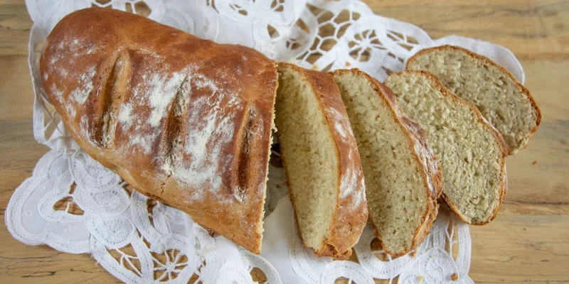 Freshly baked loaf of bread sliced and displayed on a wooden table with decorative lace
