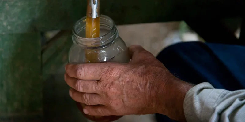 Close-up of an adult hand pouring liquid from a spout into a glass jar indoors